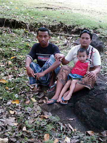 Ehepaar und kleines Mädchen sitzen auf einem Felsen in der Wiese.