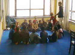 Kinder sitzen spielend im Kreis auf dem neuen blauen Teppichboden.